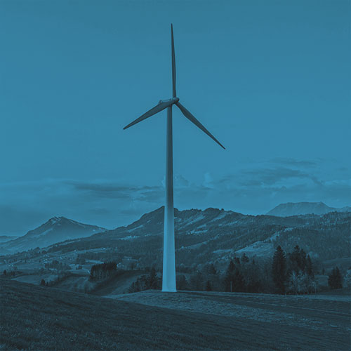 A single wind turbine stands on a grassy hill with a mountainous landscape in the background. Sustainability.