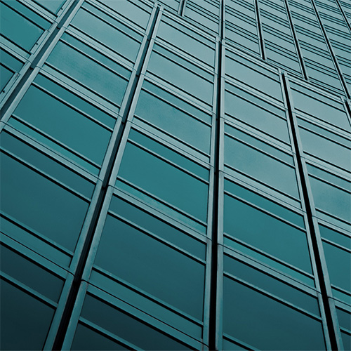 Upward view of a modern glass high-rise with teal-tinted windows against a clear blue sky.Why EAM Works Better as a Digital Twin for Enterprises.