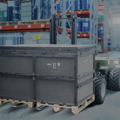 Autonomous forklift moving a large black crate on a pallet in a warehouse.
