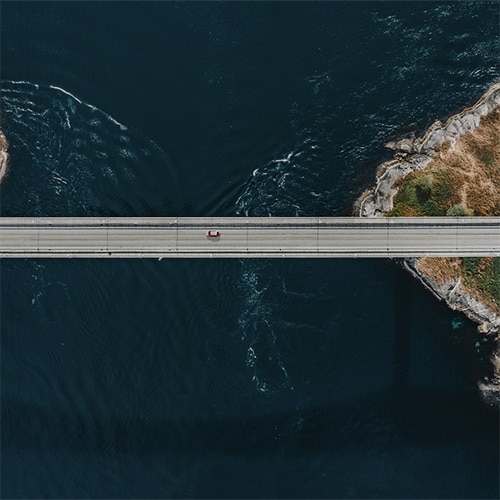 Union Pacific–Norfolk Southern Merger: Impact on US Supply Chains. Aerial view of a bridge with a red car crossing over water.