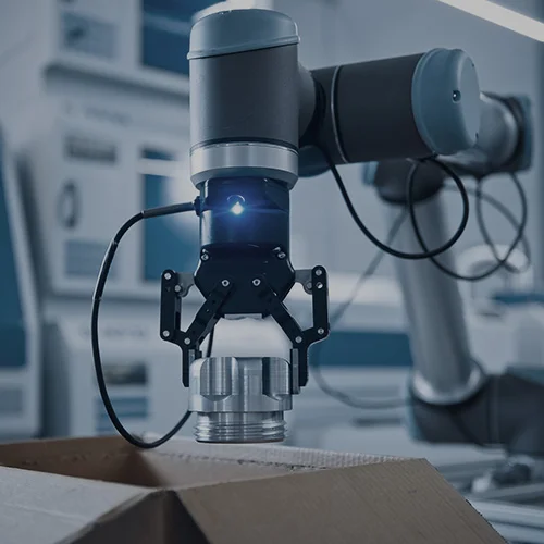 Preparing for peak seasons with SAP EWM in your warehouse. 5 Preparing for peak seasons with SAP EWM in your warehouse. Robotic arm placing a metal component into a cardboard box in a smart factory.