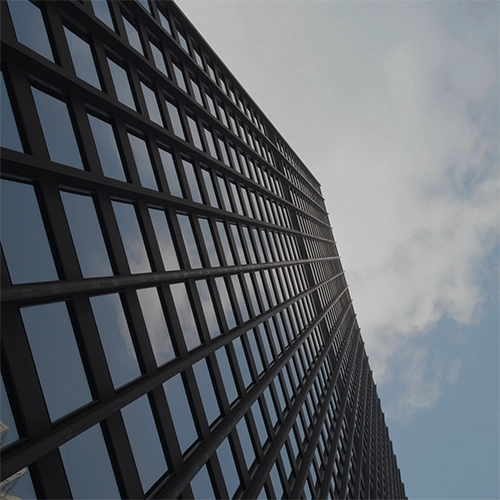 Upward view between two modern glass office buildings against a blue sky with light clouds.